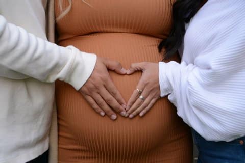 Two people's hands making a heart-like shape over a pregnant person's belly