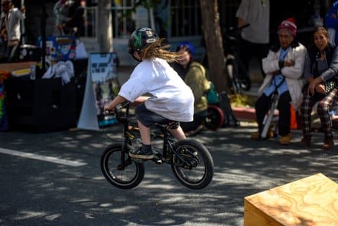 A kid with long blond hair on a mini bike airborne after coming off a small ramp