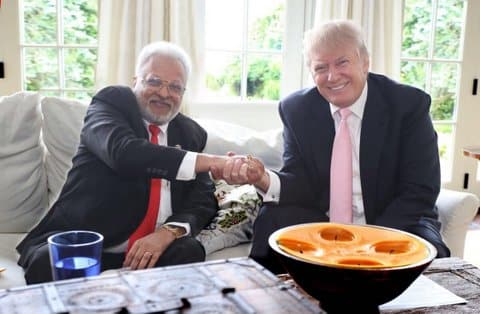 Shalabh Kumar and Donald Trump, smiling and shaking hands while sitting on a couch and facing the camera