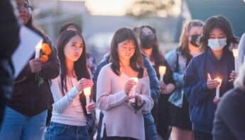 People standing together, holding candles. The picture is focused on two young Asian women