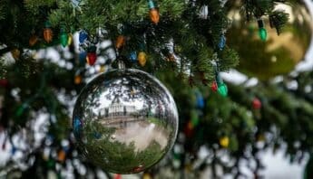 Close up of tree branches decorated with Christmas lights and ornaments included a silver ball in which the California state capitol building is reflected