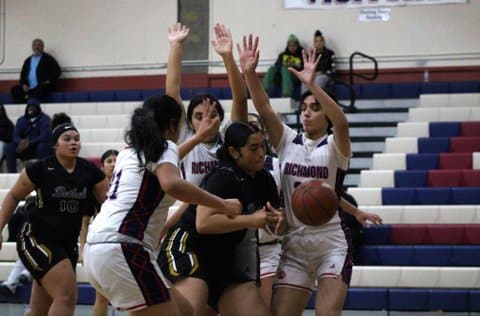 In a girls basketball game, two players stand with their arms raised above them with an opponent, teammate and loose ball in front of them