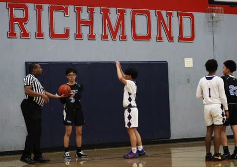 Referee holds basketball out to player as a defender stands in front of them with his arms raised