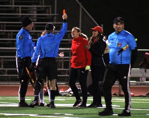 A white woman being held back by another white woman while looking with an unhappy expression at two referees, one of who is holding a red card