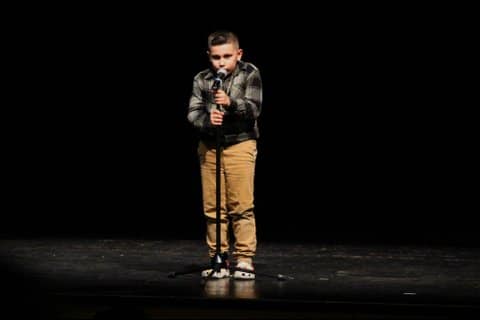 A little latino boy standing at a microphone and holding the stand