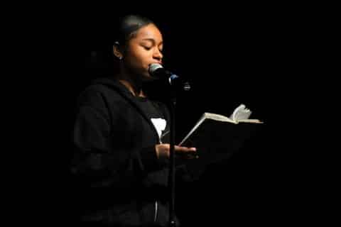 A black girl reading from a book at a microphone