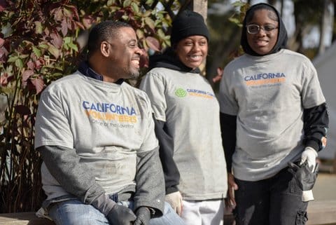 A black man and his two daughters, all wearing gray t-shirts and gloves. Two of the shirts say california volunteers office of the governor