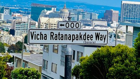 Street sign for Vicha Ratanapkdee Way that says Sonora in parentheses. Beyond the sign is a view of San Francisco