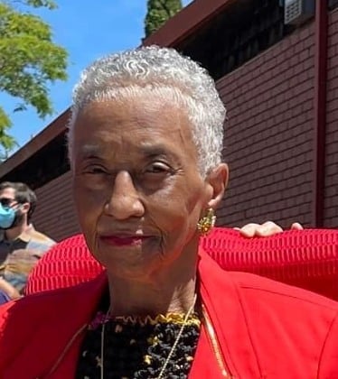 Head and shoulders shot of an older Black woman with short gray hair. She is wearing a red jacket.