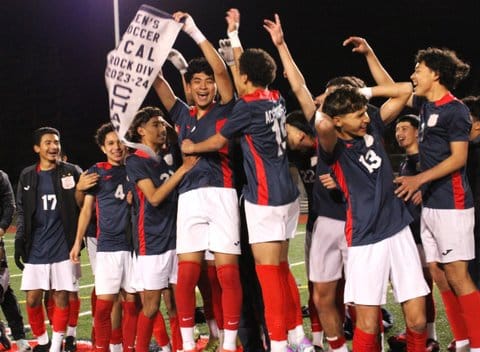 A high school boys soccer team celebrating with pennant flag championship banner