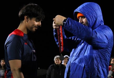 A man in blue hoodie prepares to place a medal around a Latino teen boy's neck