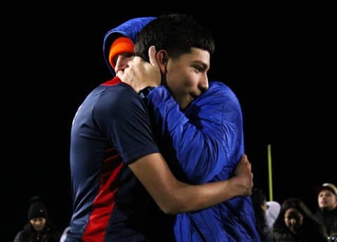 A high school soccer coach and one of his players hug.