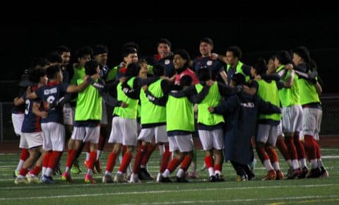 A high school boys soccer team in a big huddle surrounding one player