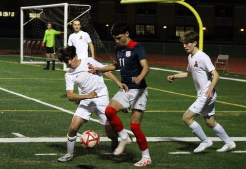 Two high school soccer players jockeying for the ball with other players looking on
