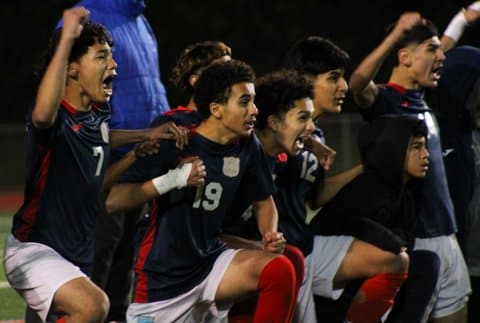 Soccer players kneeling together, some with arms raised and expressions of excitement