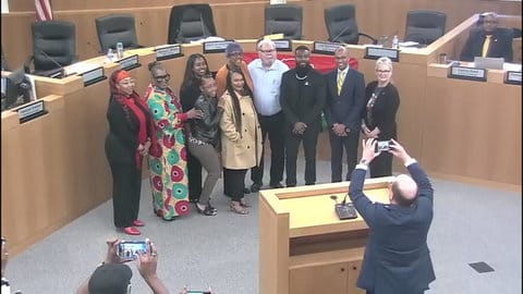 A group of six black women, two black men, a white man and a white woman pose for a group photo in Antioch city council chambers