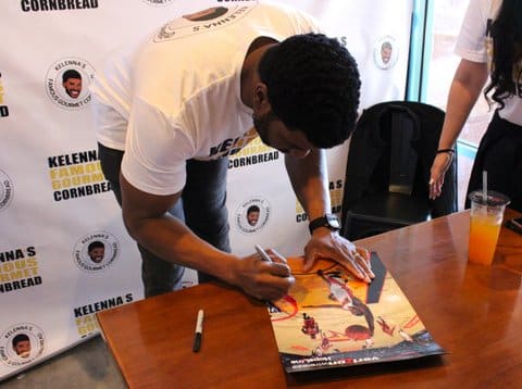 a black man autographs a photo of himself playing basketball