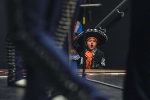 A little boy in mariachi outfit cheers from offstage