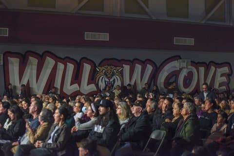 Rows of people seated in an auditorium with Willow Cove and an illustration of a wildcat painted on a wall