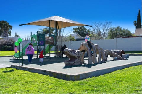 Kids on a playground with a covered play structure and a dinosaur skeleton-like structure to climb on