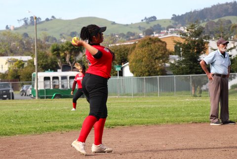 Softball player cocks her arm back to throw the ball