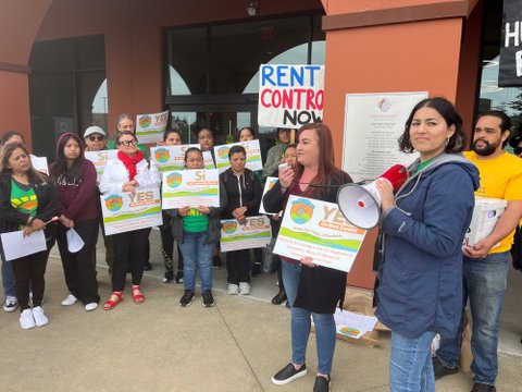 People with signs that include the message yes on rent control in english or spanish, a hand-painted sign that says rent control now and a bullhorn