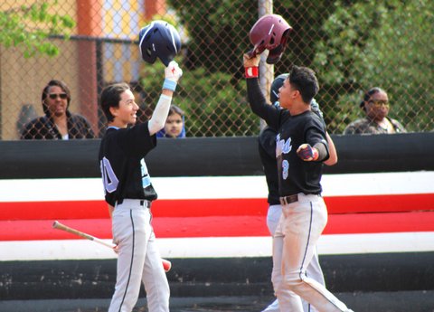 Two baseball teammates holding their helmets above their heads in celebration