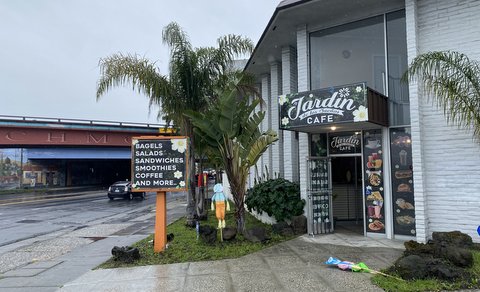 Exterior of a business with one sign that reads Jardín de los Sueños Cafe and another that reads bagels, salads, sandwiches, coffee and more. It is right next to a street heading toward an overpass that says Richmond on it.