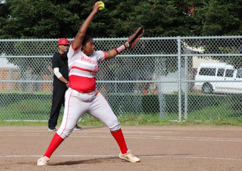 Black softball player with arms raised as she winds up to pitch