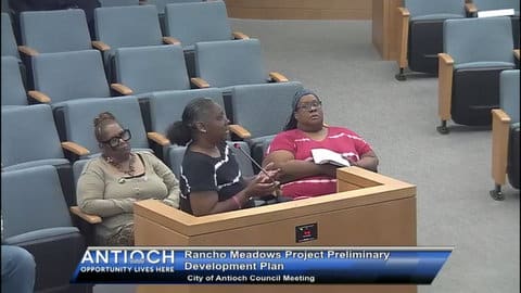 A black woman at a lectern with a microphone with two other black women seated in the front row behind her. On-screen text: rancho meadows project preliminary development plan city of antioch council meeting