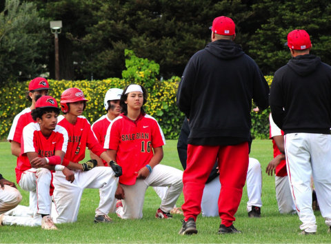 high school baseball players with displeased expressions taking a knee on the field with coaches standing in front of them with their backs to the camera