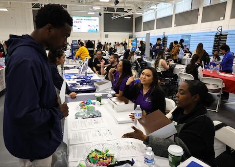 A young black man looking at a table in a career fair