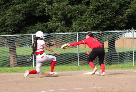 Softball player on one knee trying to slide back into first and defender with arm outstretched with ball in glove
