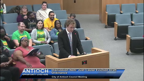 White man in suit speaks at a government meeting with other people seated behind him. Onscreen text reads Antioch opportunity lives here discussion item just cause eviction draft ordinance city of antioch council meeting