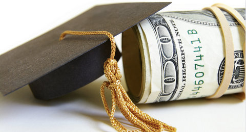 A graduation cap rested against a roll of money with a $100 bill and rubber band on the outside