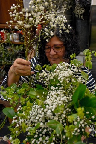 a latina woman wearing glasses and a black and white striped shirt whose face is framed by baby's breath flowers