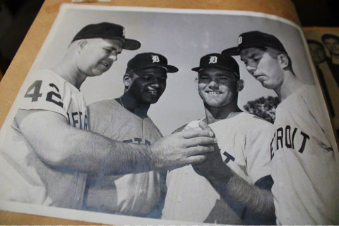 black and white photo of three white men and one black man wearing jerseys that say detroit and baseball caps with an old english D