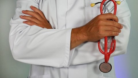 person in white lab coat standing with arms crossed and holding a red stethoscope. only their arms and part of their torso are visible