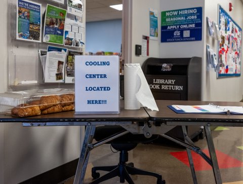 a table with a sign that reads cooling center located here, along with a roll of paper towels and a plastic container of croissants. a library book return depository is behind the table
