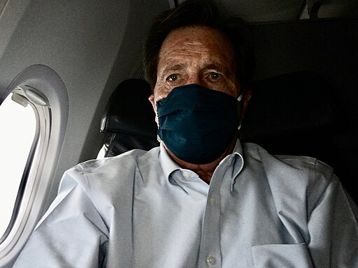 a white man on an airplane wearing a protective mask