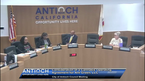 two black women, a black man and a white woman in government meeting. behind them are US and california flags and lettering on the wall that says Antioch California opportunity lives here. a chyron reads antioch opportunity lives here consideration of a cannabis operating agreement for ant green LLC city of antioch council meeting