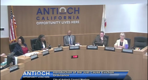 the antioch city council in meeting: two black women, a black man, a white man and a white woman. text: antioch opportunity lives here. introduction of the just cause eviction ordinance. city of antioch council meeting