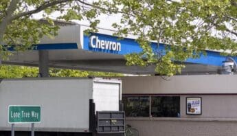 a chevron gas station awning, large white moving-style truck, road sign for lone tree way, and tree branch across the top of the photo