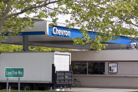 a chevron gas station awning, large white moving-style truck, road sign for lone tree way, and tree branch across the top of the photo