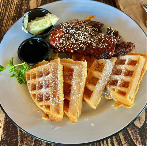 plate with four triangular waffle slices and glazed fried chicken dotted with sesame seeds