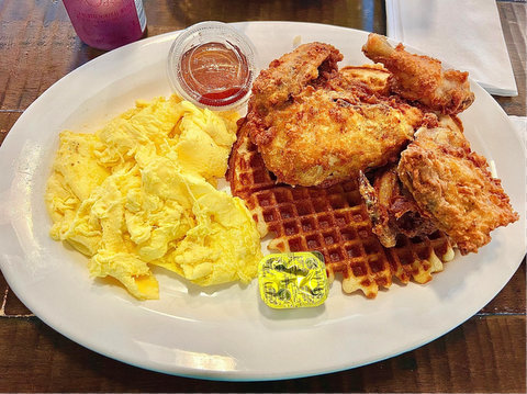 a plate of scrambled eggs, waffle, fried chicken and syrup