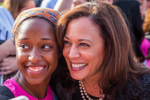 head and shoulders shot of a young black woman, possibly in her teens, and kamala harris standing side by side, their heads touching and both smiling