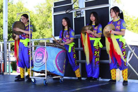 four chinese teen girls in colorful costumes. two have cymbals and one is at a large drum