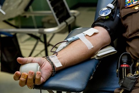 close up of the arm of a law enforcement official donating blood. they are in uniform and holding an object to squeeze with a blood pressure cuff on their upper arm and tubing taped to his arm