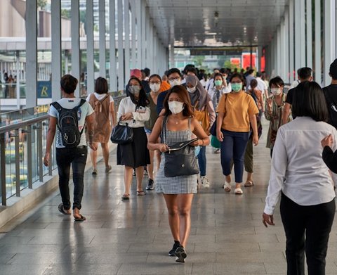 crowd of people going down a walkway, several wearing protective face masks